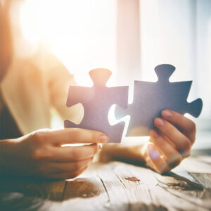 To hænder, der holder hver sin puslespilsbrik klar til at samle dem.